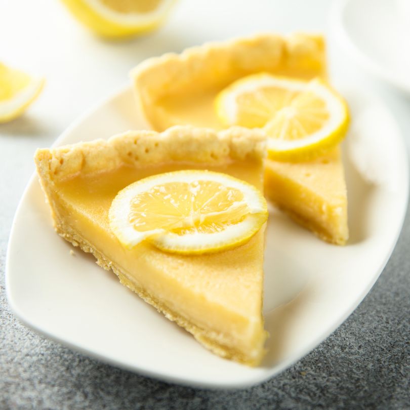 Zwei Stücke einer Low Carb Passionsfrucht Lemon Tarte mit goldgelber Füllung und knusprigem Rand, serviert auf einem weißen Teller, garniert mit frischen Zitronenscheiben.