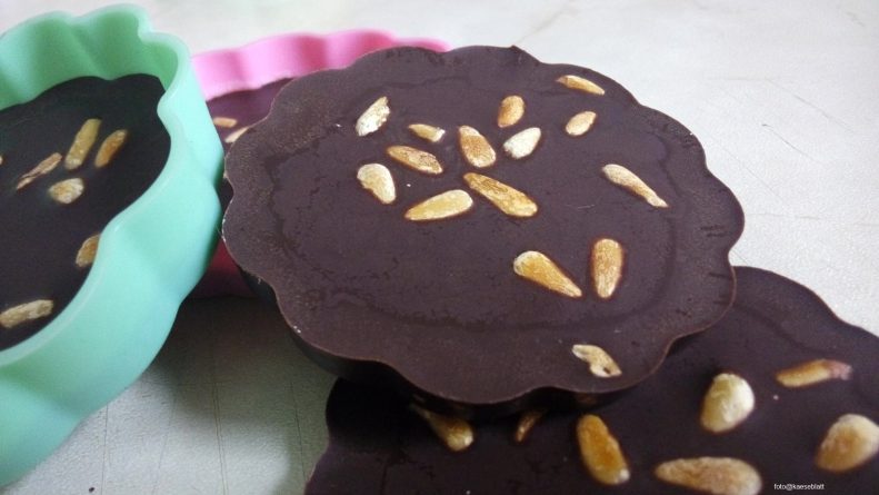 Keto Schokolade selber machen – Zartbitterschokolade mit gerösteten Pinienkernen auf einem Teller, zuckerfrei und selbstgemacht

