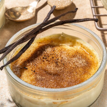 Nahaufnahme einer Keto Kokos Crème Brûlée in einem Glasbehälter mit karamellisierter Oberfläche, garniert mit Vanilleschoten.
