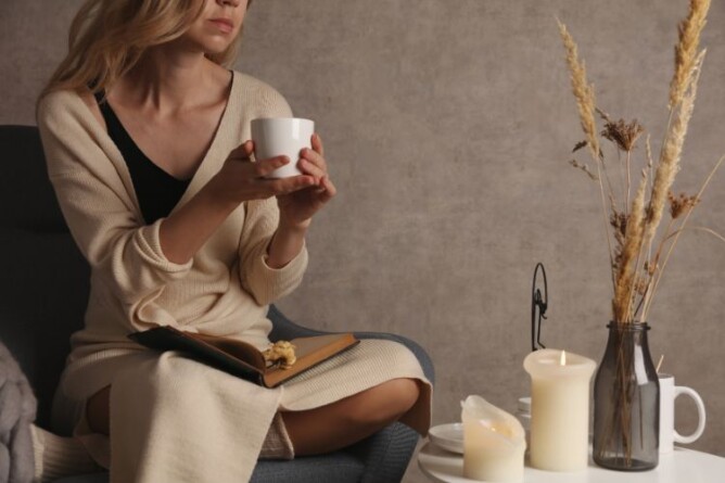 Eine nachdenkliche Frau sitzt gemütlich mit einer Tasse Tee und einem offenen Notizbuch in der Hand. Das Bild symbolisiert Selbstreflexion, Achtsamkeit und Journaling als Wege, um das eigene Körperbild nach Gewichtsverlust bewusst wahrzunehmen.
